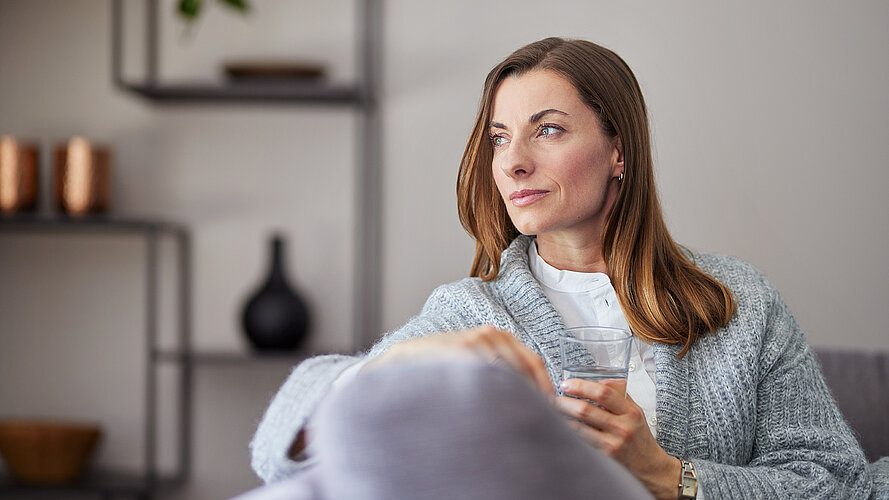 Frau sitzt auf der Couch und schaut in den Raum