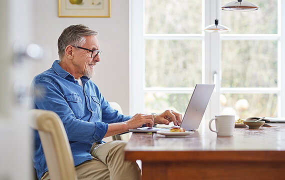 Mann sitzt am Esstisch und arbeitet am Laptop