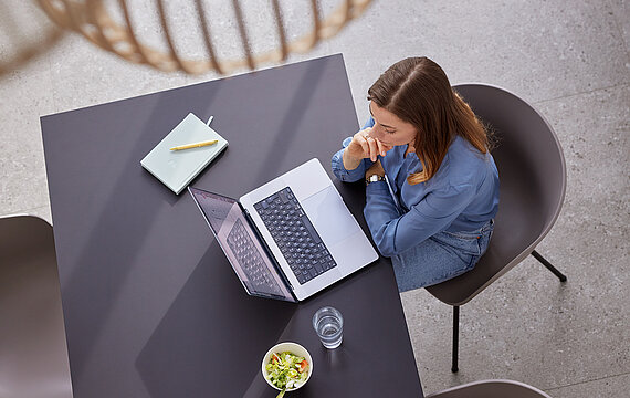 Frau sitzt am Esstisch und schaut in ihr Macbook