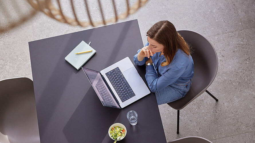 Frau sitzt am Esstisch und schaut in ihr Macbook